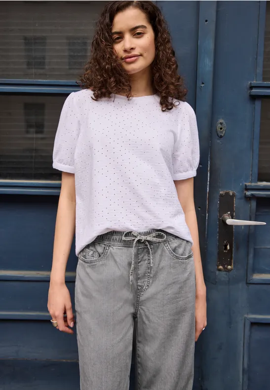 Person mit weißer Bluse und grauer Hose steht vor blauem Türportal.
