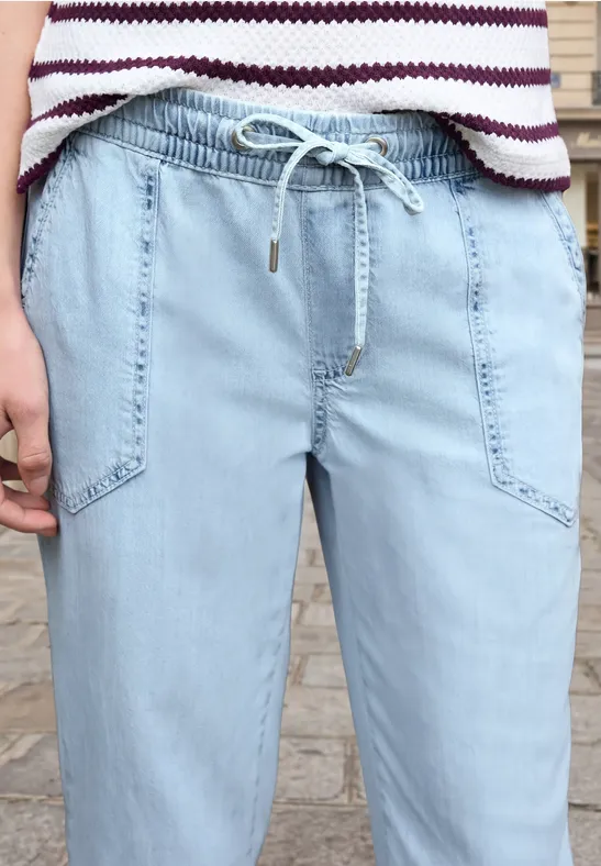 Lichtblauwe jeans met koordsluiting en opgestikte zakken, gecombineerd met een gestreept shirt.