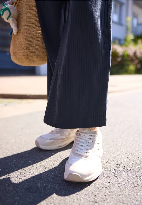 Weiße Sneaker, weite dunkelblaue Hose, Basttasche, sonnige Straßenszene.