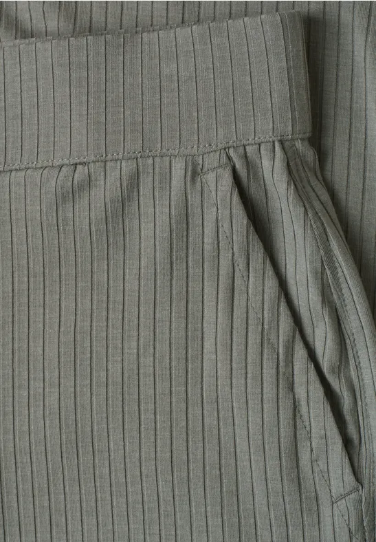 Detailaufnahme einer graugrünen, gerippten Stoffhose mit elastischem Bund und seitlicher Tasche.