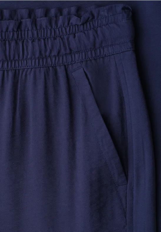 Close-up van een donkerblauwe broek met elastische tailleband en zijzak.