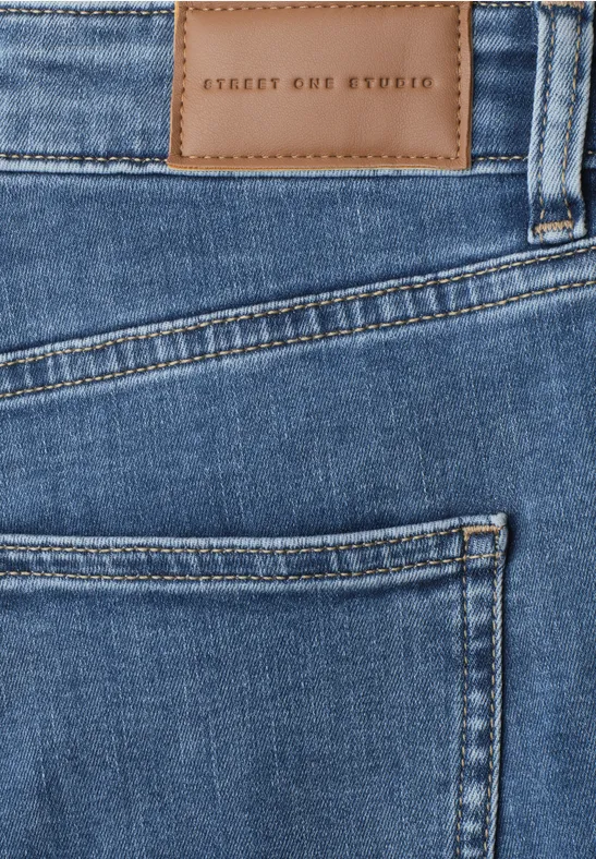 Gros plan sur un jean bleu avec poche arrière et étiquette en cuir 'STREET ONE STUDIO'.