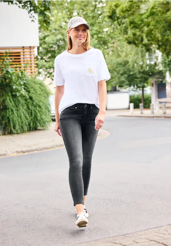 Eine junge Frau spaziert entspannt auf der Straße und hält ein Skateboard.