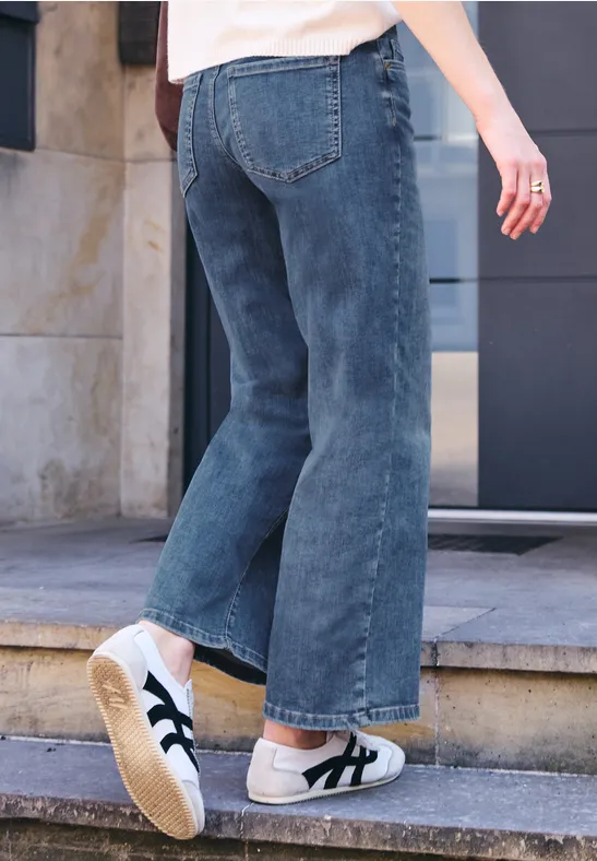 Une personne en jean et baskets blanches monte une marche d'escalier à l'extérieur.