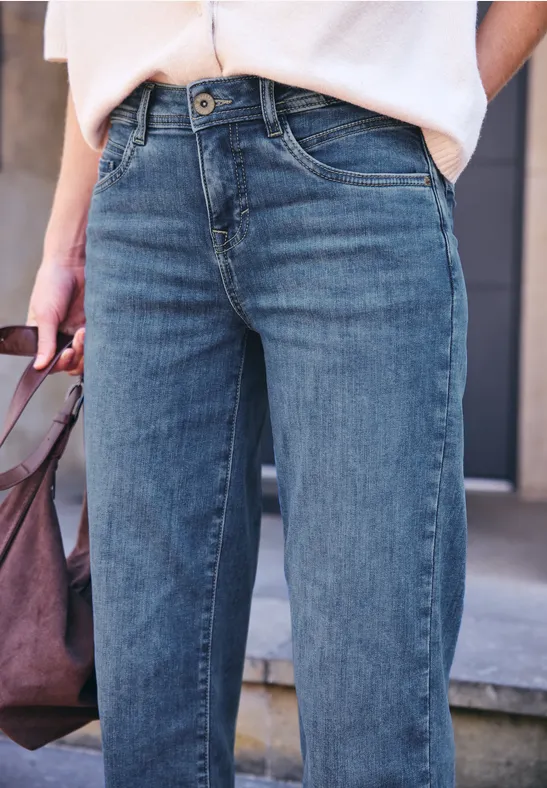 Personne porte un jean bleu et haut blanc, tient un sac à main et se tient devant des marches.