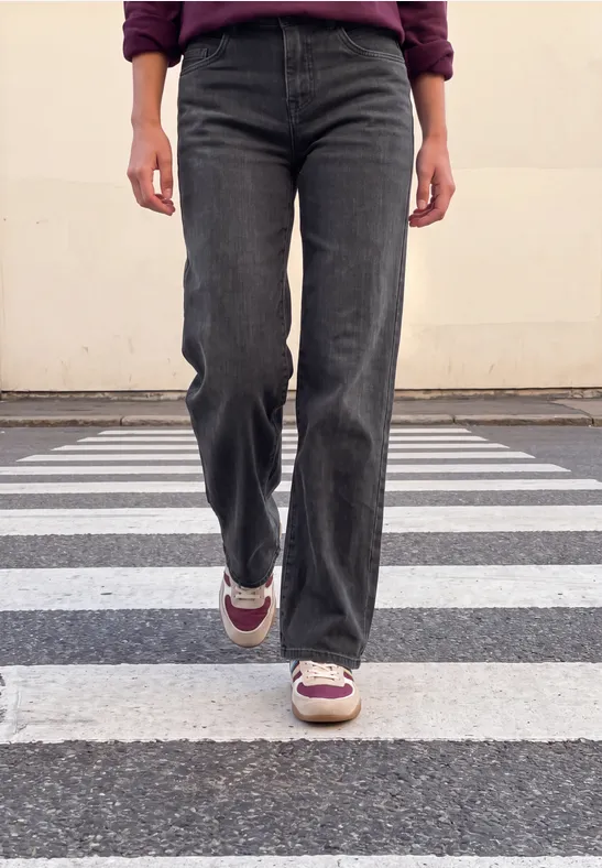 Eine Person in schwarzen Jeans und Sneakers läuft über einen Zebrastreifen, nur die Beine sichtbar.
