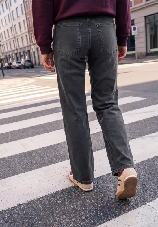 Eine Person in grauen Jeans und weinrotem Pullover überquert auf einem Zebrastreifen eine Straße.
