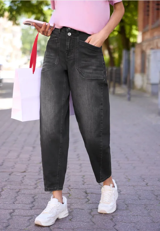 Person trägt schwarze baggy Jeans, pinkes Oberteil, weiße Sneaker und geht auf einem Gehweg.