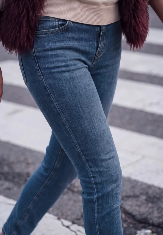 Jemand in engen blauen Jeans überquert einen Zebrastreifen.