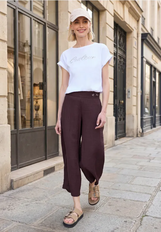 Person mit weißem T-Shirt und weiten, braunen Hosen läuft auf gepflasterter Straße an Hausfronten vorbei.