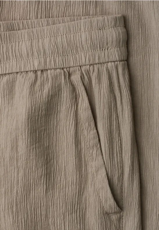 Detailaufnahme einer beigen Crinkle-Stoffhose mit elastischem Bund und seitlicher Tasche