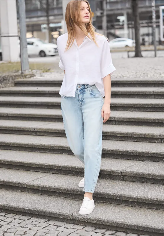 Frau in weißem Hemd und Jeans läuft lässig Treppe hinab in urbaner Umgebung.