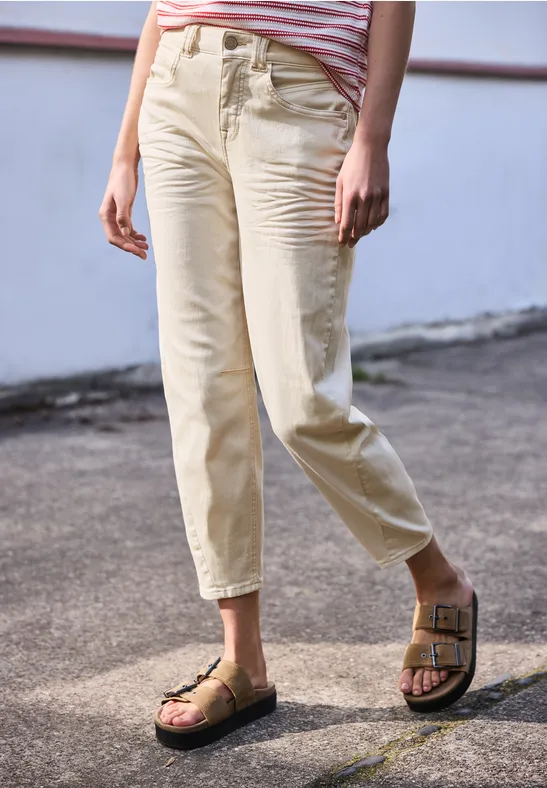 Iemand staat buiten in lichtgekleurde broek tot de enkels en bruine sandalen met gespen.