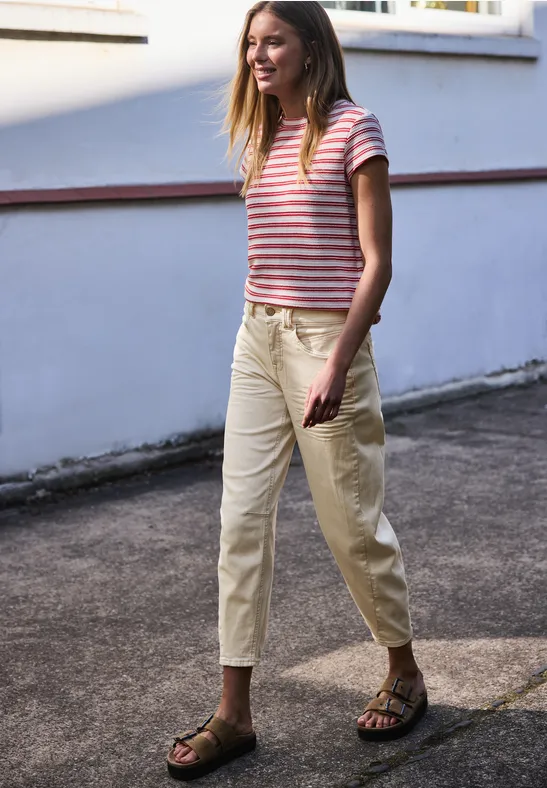Vrouw in gestreept T-shirt en lichte broek die over een geplaveid pad loopt.