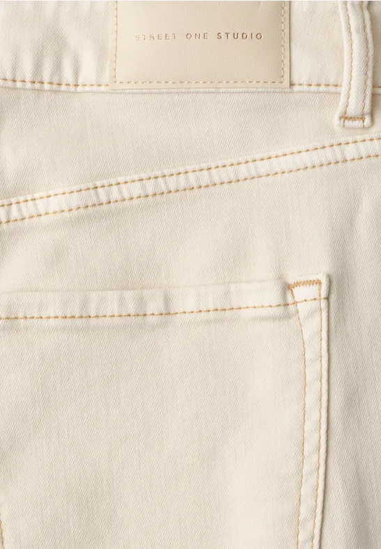 Close-up van een lichtbeige spijkerbroek met zak en zichtbare naden.