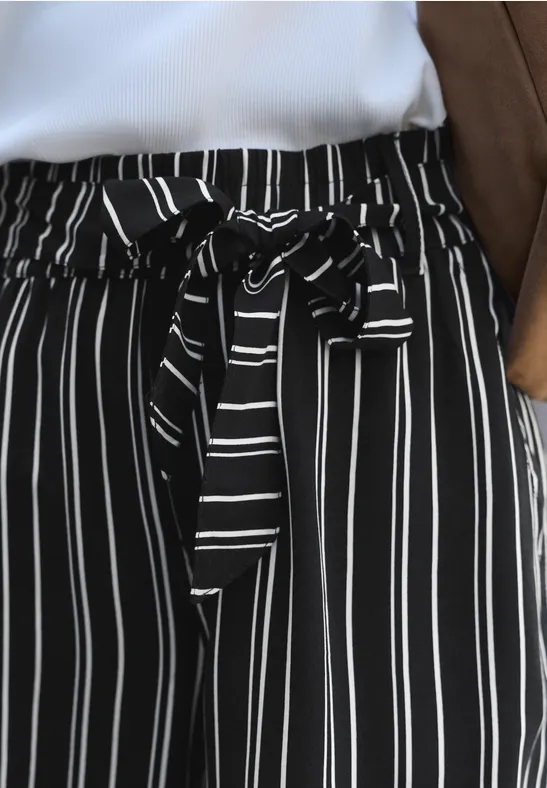 Zwarte wijde broek met witte verticale strepen en een strikceintuur in de taille.