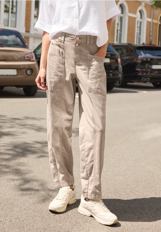 Person steht auf der Straße, trägt weiße Bluse, lockere beige Hose und weiße Sneakers.
