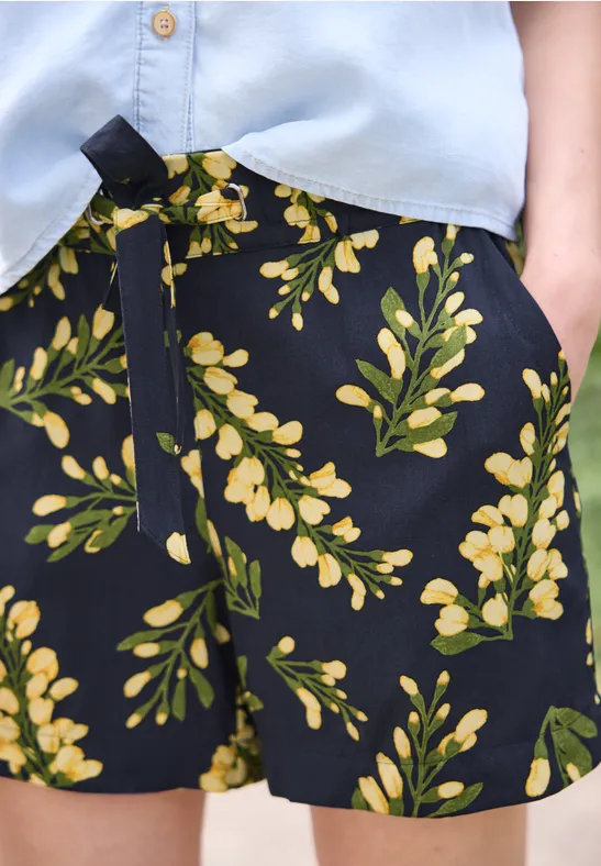 Shorts noirs à imprimé floral jaune et vert avec cordon de serrage, portés avec un haut bleu clair.