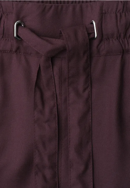 Close-up van een bordeauxrode tailleband met geïntegreerde stoffen riem en zilverkleurige oogjes
