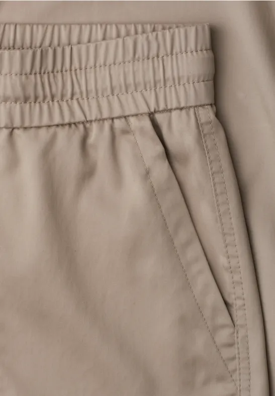 Nahaufnahme einer beigen Hose mit elastischem Bund und schräger Tasche.