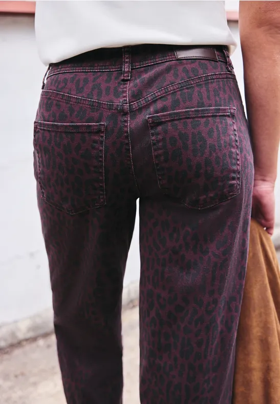 Nahaufnahme einer Person von hinten in hoch taillierten, lila Leoparden-Jeans, dazu weißes Oberteil und braune Tasche.