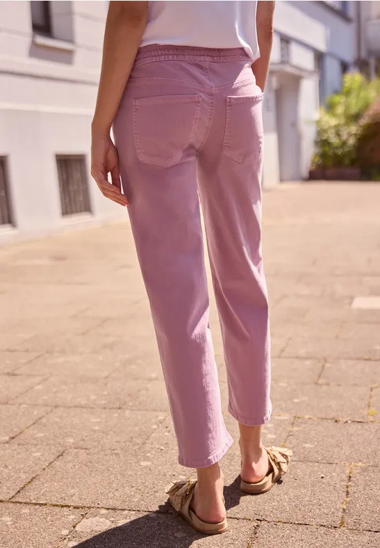 Frau von hinten in rosa Hose und Sandalen läuft auf sonnigem Gehweg.