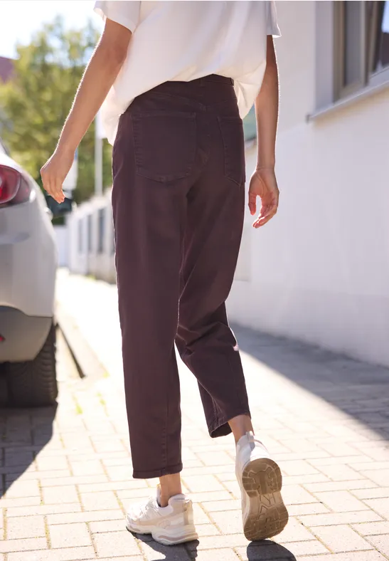 Person mit weißen Sneakern und dunkelbraunen Hosen läuft auf dem Gehweg an einem weißen Haus vorbei.