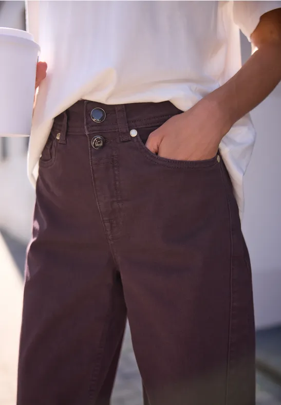 Nahaufnahme einer Person in braunen Jeans mit Hand in Tasche und Kaffeebecher.