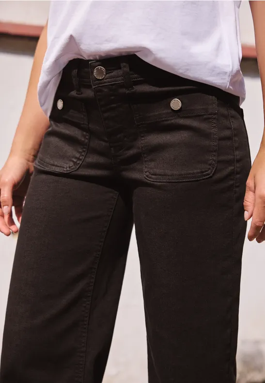 Close-up einer Person in schwarzen High-Waist-Jeans und weißem Shirt, Hände locker an den Seiten