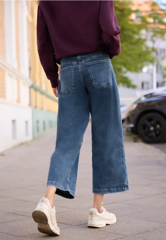Eine Person läuft auf dem Gehweg in weiten, knöchelhohen Jeans und weißen Sneakers.