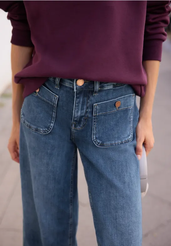 Nahaufnahme einer Person in blauen Jeans mit auffälligen Taschen und lila Pullover.