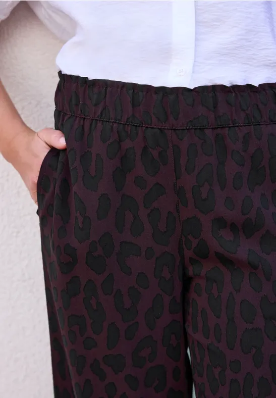Pantalon à motif léopard noir, taille élastique et main dans la poche, associé à un chemisier blanc