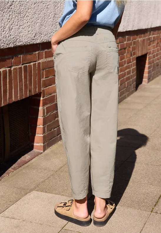 Rückansicht einer Person in beige Hosen und Sandalen auf einem Bürgersteig vor einer Backsteinwand