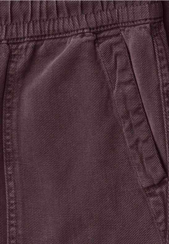 Close-up van een donkerrode joggingbroek met elastische tailleband en zijzak.