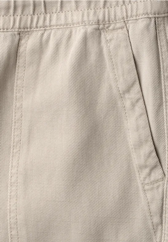 Close-up van een beige stoffen broek met elastische taille en zijzak.