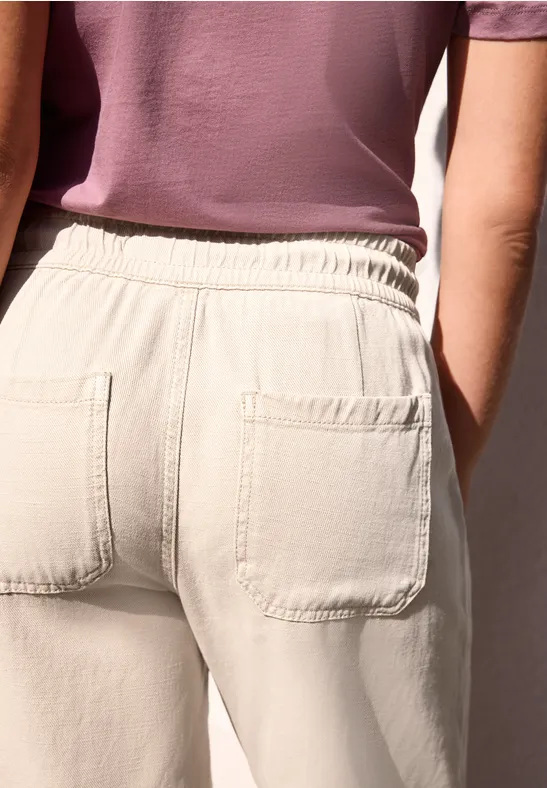 Rugaanzicht van een persoon in beige broek met opgestikte achterzakken en een paars shirt