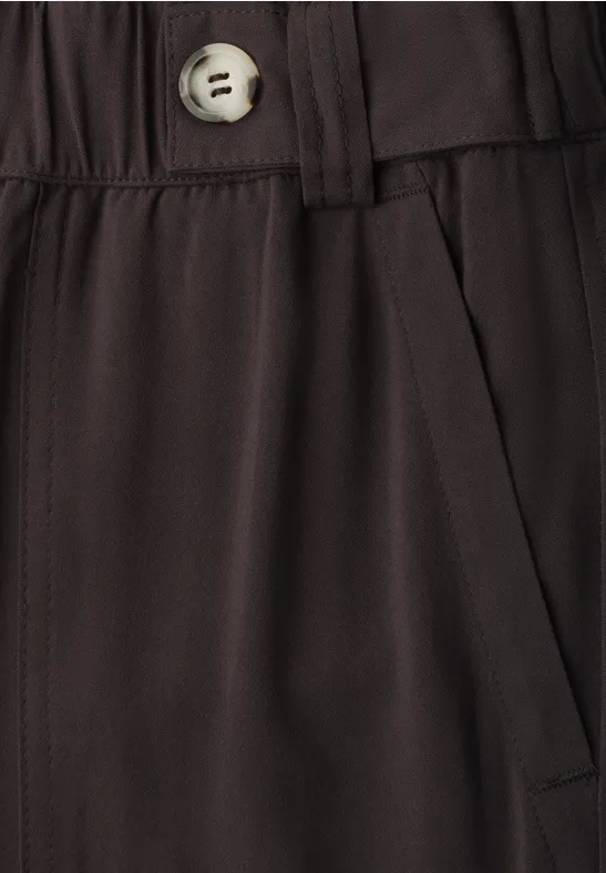 Gros plan d’un pantalon sombre avec taille élastique, poche latérale et bouton clair.