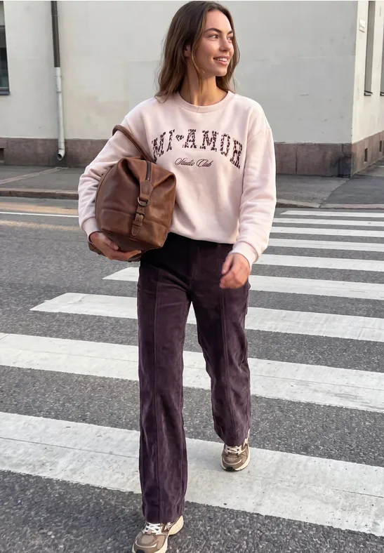 Une femme décontractée traverse un passage piéton avec un sac marron, souriante et élégante.