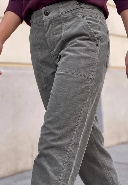 Graue Cordhose in lässigem Schnitt, getragen von Person mit dunklem Oberteil, vor urbanem Hintergrund.