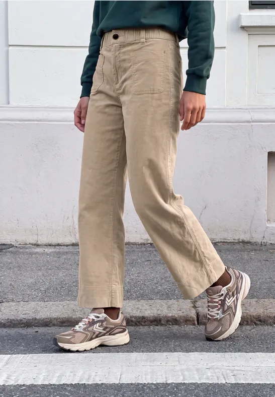 Person geht über Zebrastreifen, trägt beige weite Hose, gemusterte Sneaker und grünen Pullover.