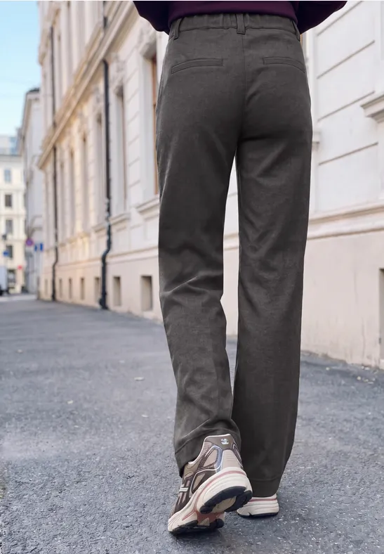 Persoon in grijze vrijetijdsbroek en sneakers loopt over een stadsstraat met historische gevels.