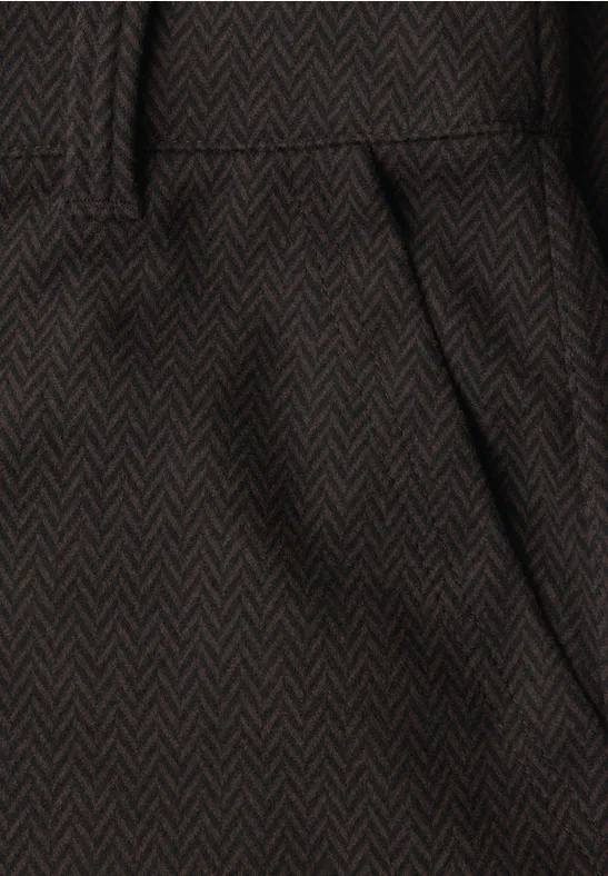 Detail van een donkerbruin visgraatbroek met schuine zak en tailleband.