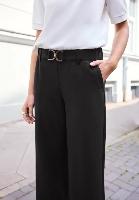 Schlanke, weit geschnittene schwarze Hose mit modischem Gürtel und weißem Oberteil, lässig und elegant.