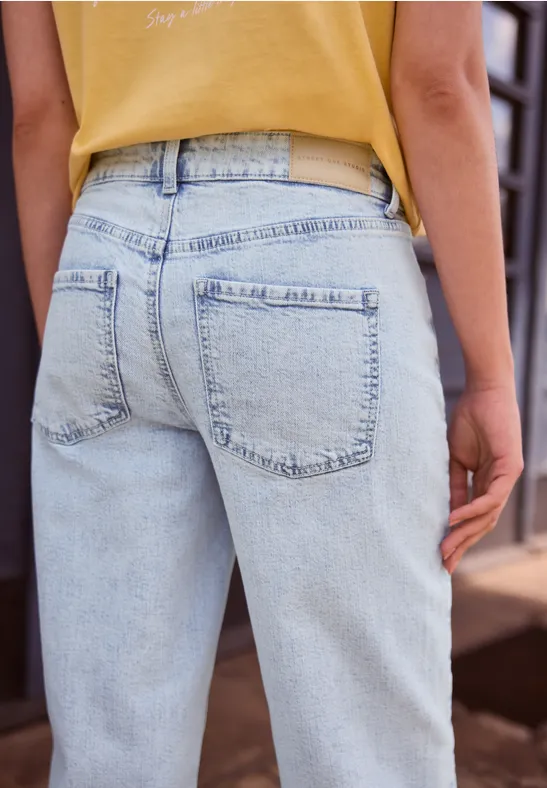 Person von hinten in hellblauen Jeans und gelbem Top, im urbanen Umfeld