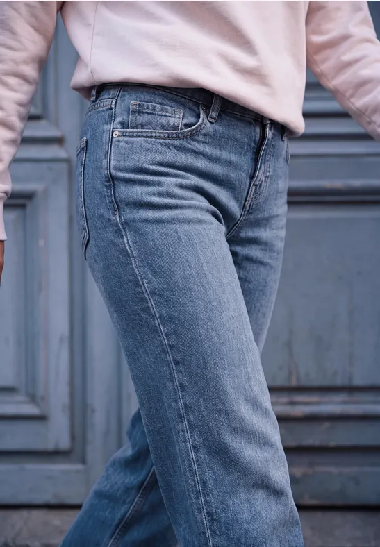 Unterkörper in blauen Jeans und hellem Oberteil vor einer klassischen Türkulisse.