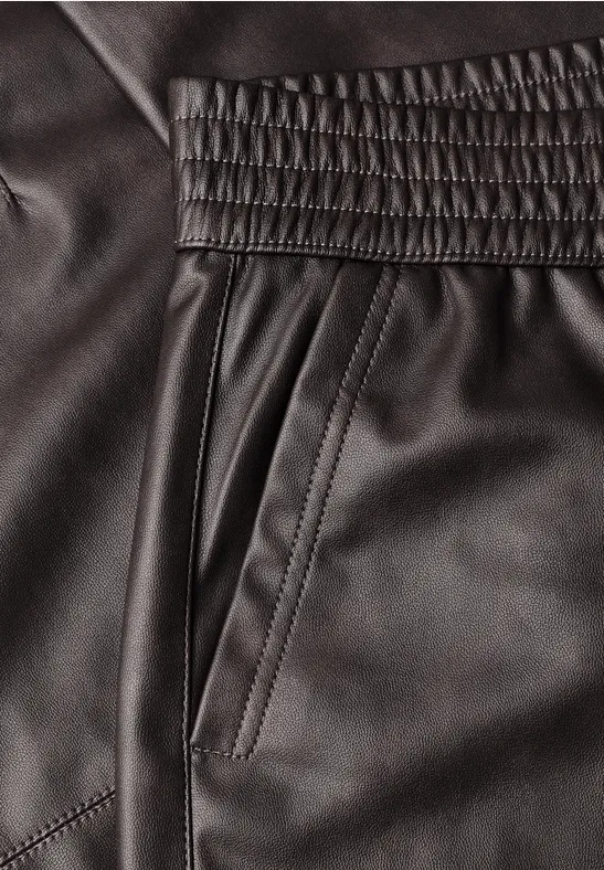 Detailaufnahme schwarzer Lederhose mit Gummibund, seitlicher Tasche und Ziernähten.