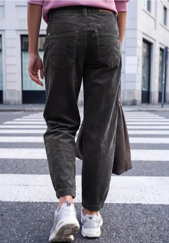 Vue arrière d’une personne en pantalon vert et baskets blanches traversant un passage piéton urbain.