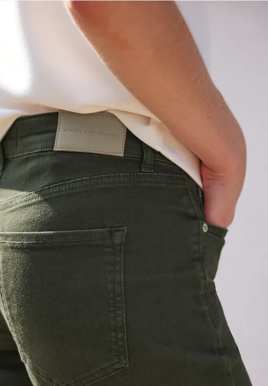 Rückansicht einer Person in olivgrünen Jeans und weißem Oberteil mit einer Hand in der Gesäßtasche.