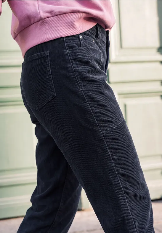 Seitliche Ansicht einer Person in schwarzen Jeans und rosa Pullover vor hellgrüner Wand.