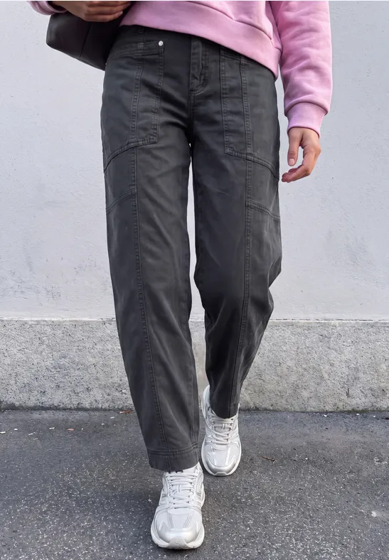 Eine Person geht auf dem Gehweg, trägt dunkelgraue Hosen, weiße Sneaker und einen rosa Pullover.
